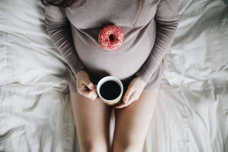 vrouw zwanger op bed met tas koffie en donut