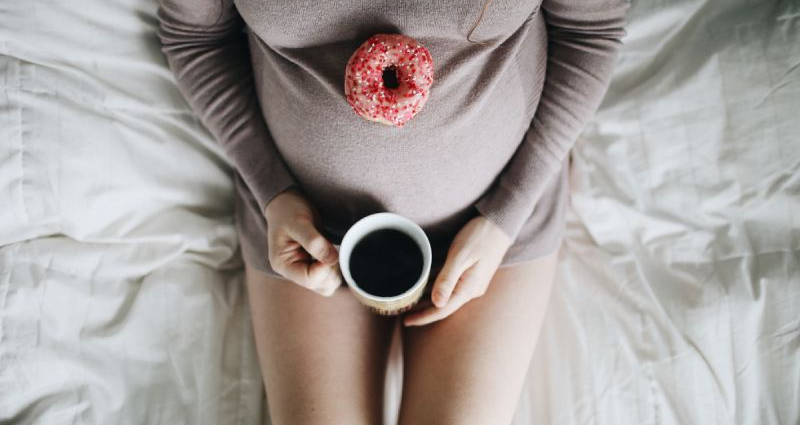 vrouw zwanger op bed met tas koffie en donut